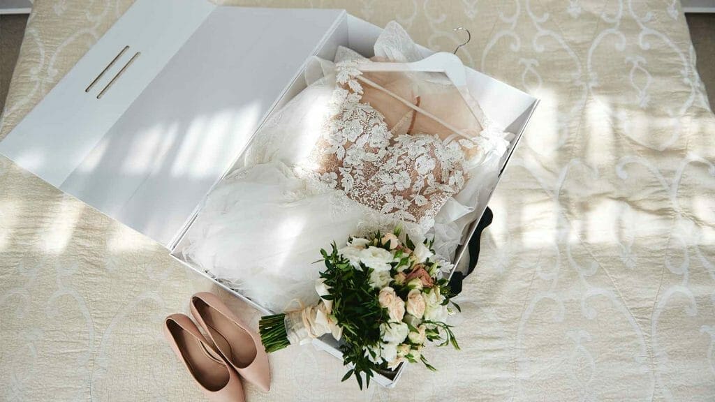 A wedding dress and shoes in a box on a bed.