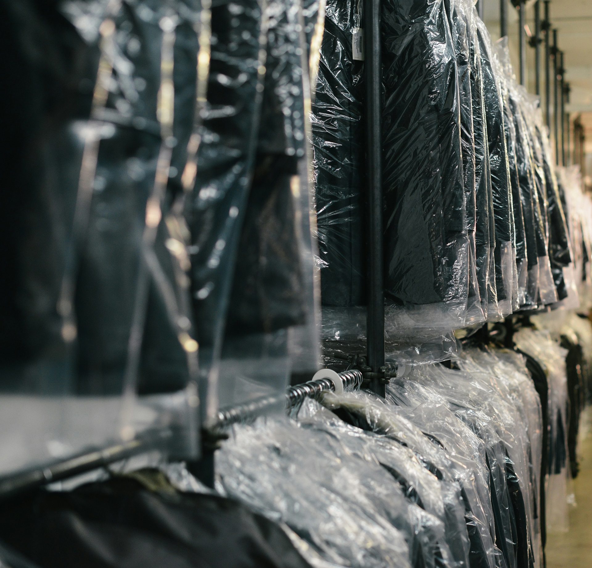 Row of clothing items covered in plastic garment bags hanging on a rack.