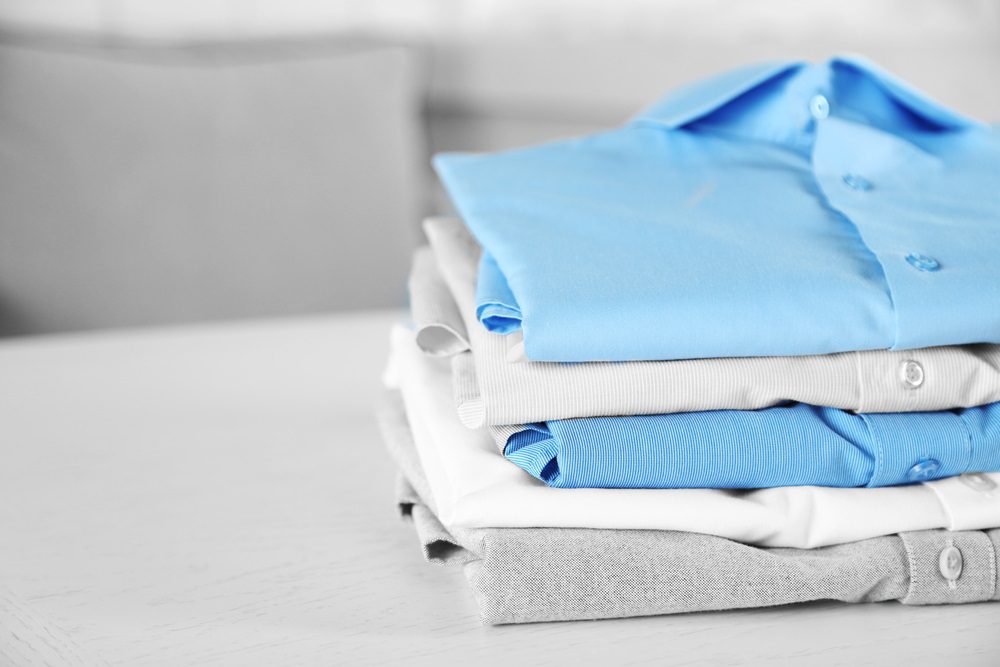 A neatly folded stack of shirts in varying shades of blue, gray, and white rests on a white surface.