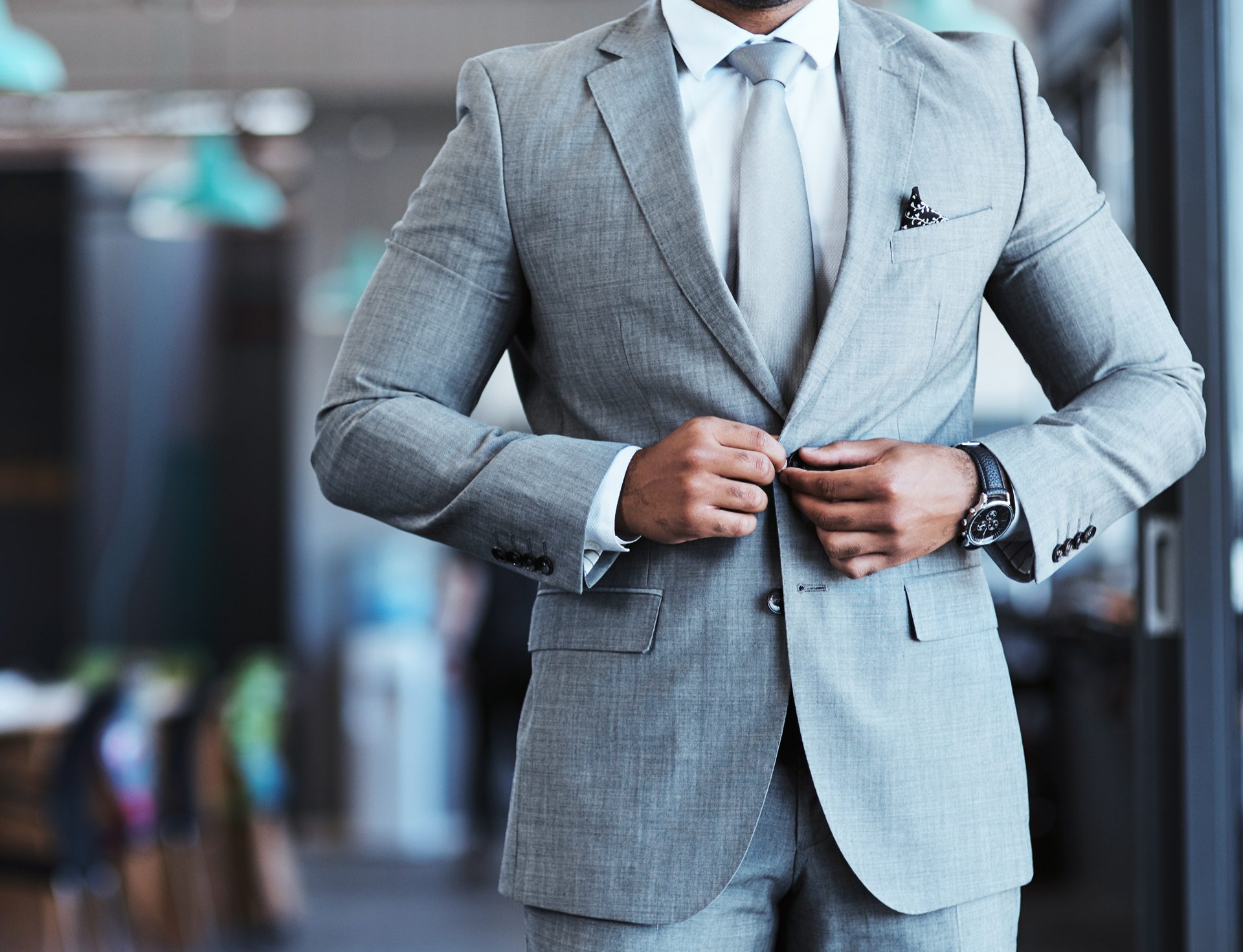 A person in a grey suit fastens their jacket button.
