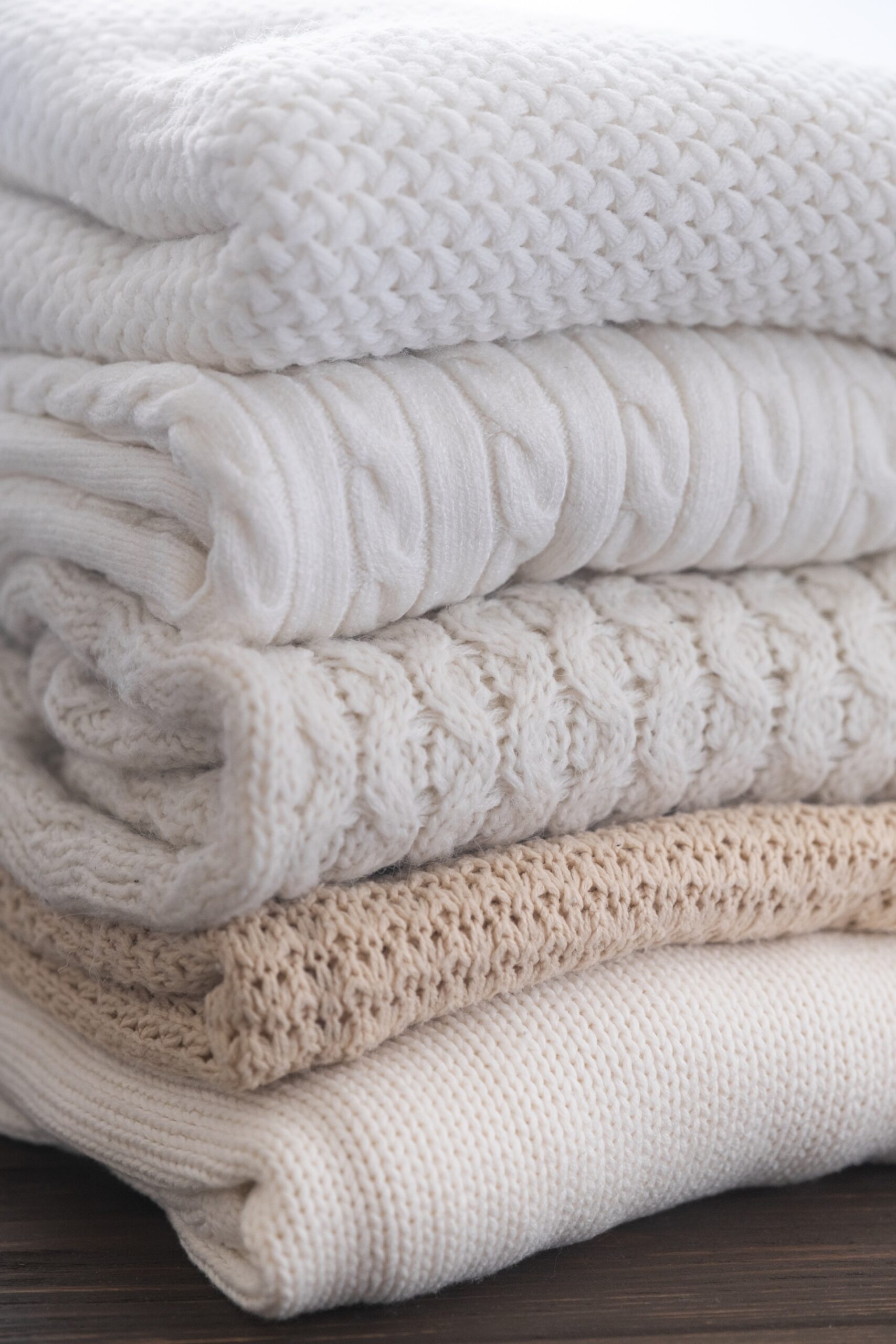 A stack of neatly folded cream and beige knit sweaters on a wooden surface.