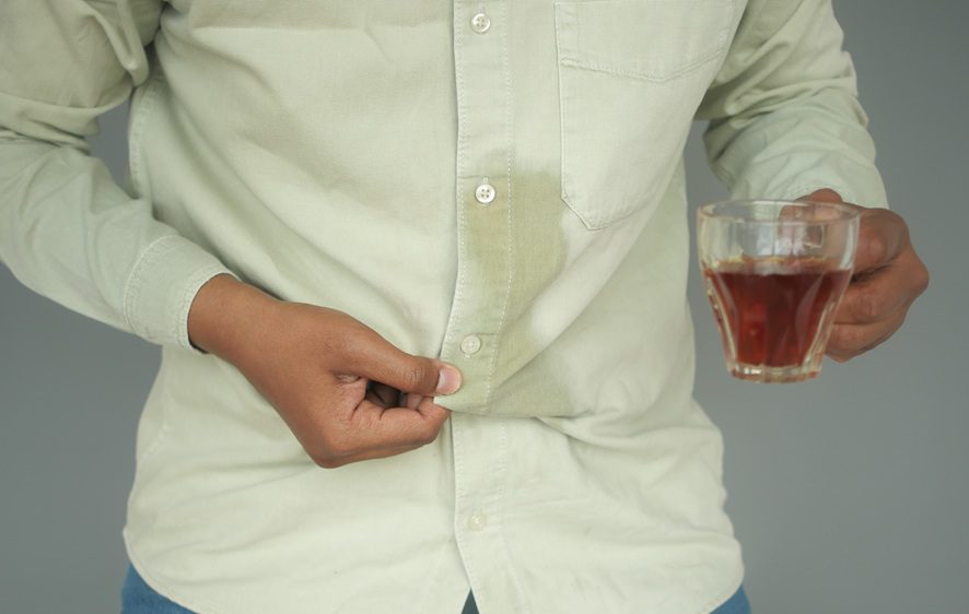 A person holding a glass of tea with a visible stain on their light-colored shirt.