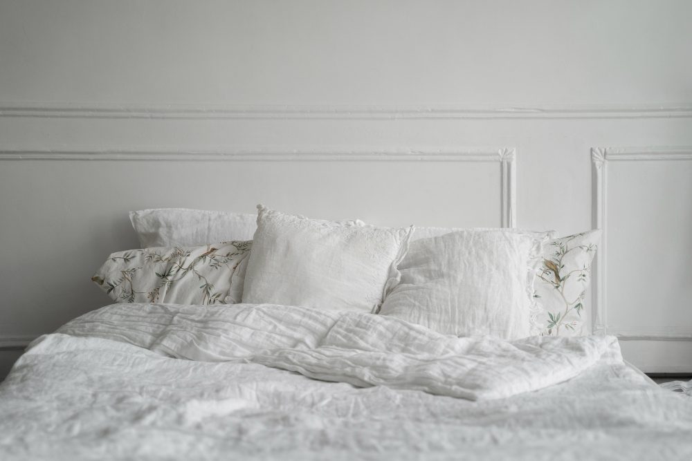 A neatly made bed with white linens and a mix of plain and patterned pillows against a white wall with decorative molding.