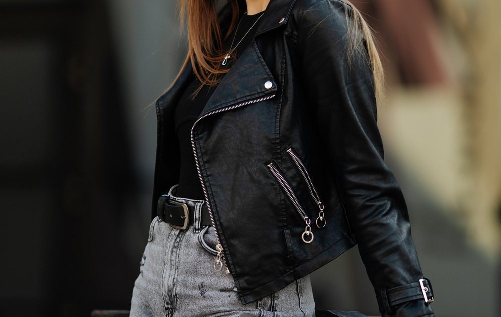 Person wearing a black leather jacket, black shirt, and high-waisted gray jeans with a black belt; background out of focus.